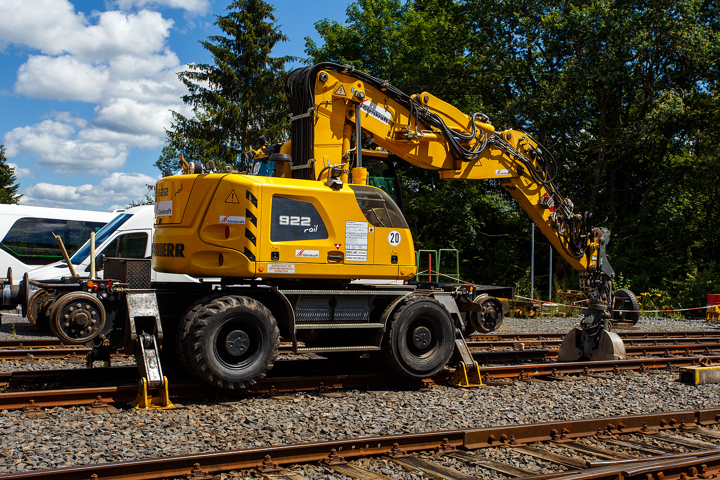 Liebherr Zweiwegebagger A 922 Rail Litronic) mit Abstützpratzen, Kleinwagen Nr. D-WJSLK 99 80 9903 403-0, der Gleiskraft GmbH (Ulmen), abgestellt am 07 Juli 2024 auf dem Betriebshof der Westerwaldbahn (WEBA) auf der Bindweide bei Steinebach/Sieg.

Der A 922 Rail Litronic kann als Zweiwegemaschine wahlweise auf der Straße oder auf Eisenbahnschienen eingesetzt werden. An beiden Seiten des Unterwagens ist das Schienenfahrwerk angebracht. Während des Aufgleisens bringt das Schienenfahrwerk die Bereifung auf Schienenniveau, wobei die inneren Räder der Zwillingsbereifung den Fahrantrieb auf der Schiene übernehmen.

TECHNISCHE DATEN:
Spurweite: 1.435 mm (Normalspur)
Länge über Puffer: 6.400 mm
Achsabstand (Schiene): 5.700 mm
Laufraddurchmesser (Schiene): 500 mm (neu)
Eigengewicht: 23 t
Motorbauart: wassergekühlter 4Takt - 4-Zylinder-Reihendieselmotor mit Common-Rail-Einspritzsystem, Turbolader und Ladeluftkühlung
Motortyp: Liebherr D924 – FPT
Motorhubraum: 4,5 Liter
Motorleistung: 120 kW / 163 PS
Höchstgeschwindigkeit (Hg): 20 km/h (in Kreuzungen und Weichen 10 km/h)
Zugkraft: 117 kN
Bremse: Kfz.-/SFE-Bremse und Wagonbremsanlage
Zul. Anhängelast: 120 t (ungebremst 40 t)
Zur Mitfahrt zugel. Personenzahl: 1 (und Fahrer)
Antrieb auf Schiene: Über Reibantrieb der Straßenreifen
Hinterer Schwenkradius: 2.000 mm
Max. Neigung: 40 ‰